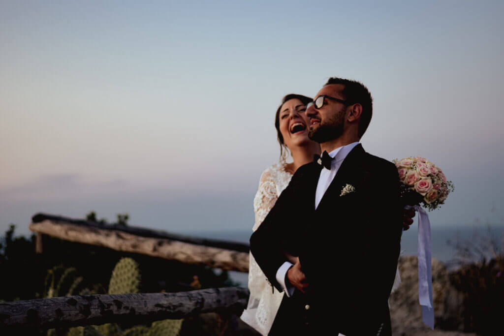 Et lykkelig brudepar ler sammen under solnedgangen. Fotografert av Anna O. Brambilla, en erfaren bryllupsfotograf. A joyful bride and groom laughing together at sunset. Captured by Anna O. Brambilla, an experienced wedding photographer