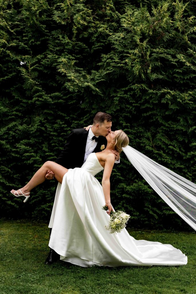 Brudepar som omfavner hverandre i en hage, med slør i bevegelse og elegant brudekjole