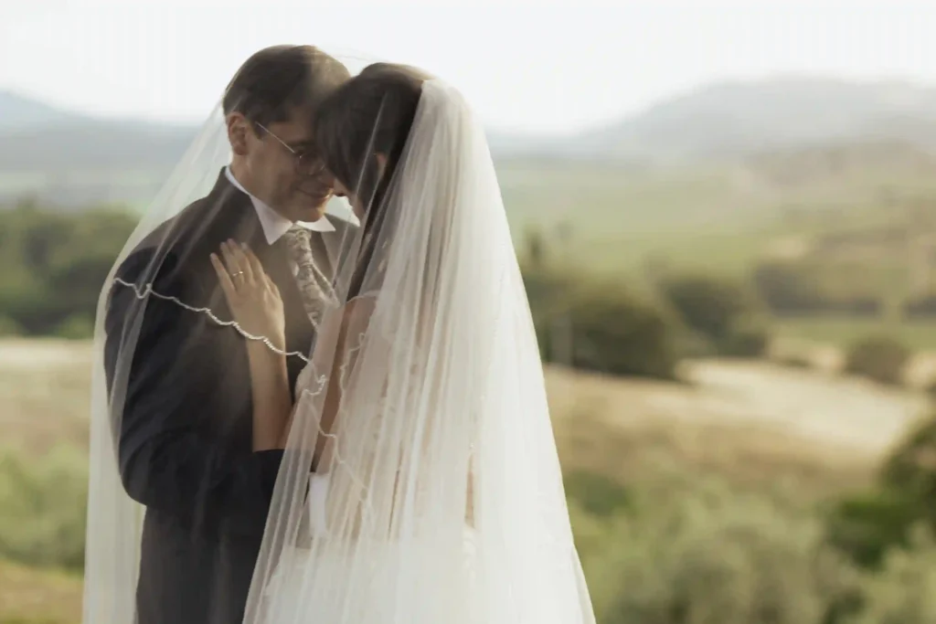Brudepar står tett omslynget under sløret med utsikt over det toskanske landskapet. Intimt øyeblikk fanget under et bryllup i Toscana. Foto av bryllupsfotograf Anna O. Brambilla