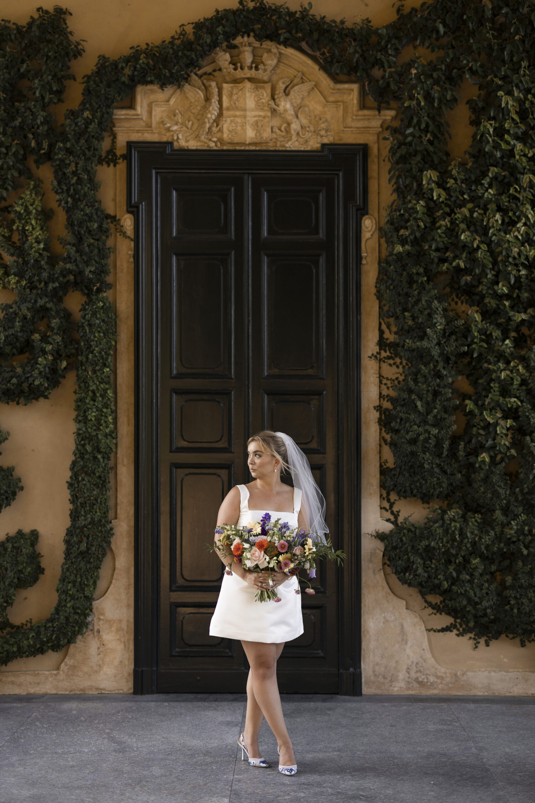 Bride holding a colorful bouquet in front of an ornate doorway at Villa del Balbianello during her elopement in Varenna. Photo by wedding photographer Anna O. Brambilla. Brud med fargerik blomsterbukett foran en dekorativ dør på Villa del Balbianello under elopement i Varenna. Foto av bryllupsfotograf Oslo Anna O. Brambilla.