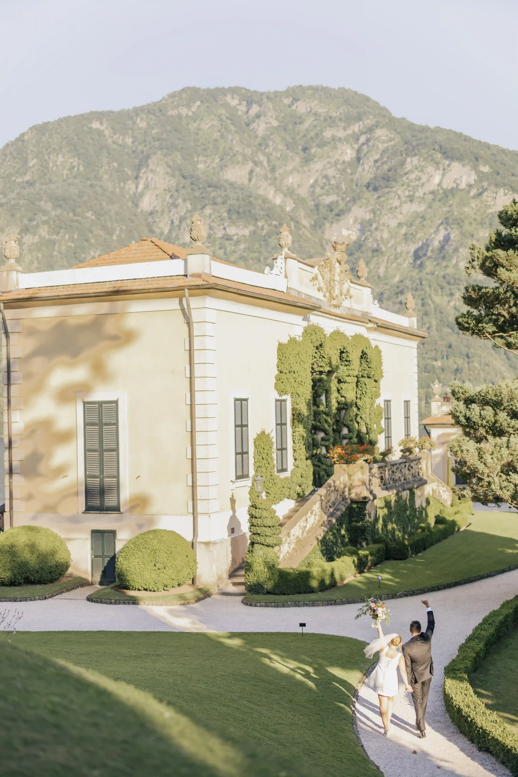 Bride and groom walking hand in hand through the gardens of Villa del Balbianello, celebrating after their elopement in Varenna. Photo by wedding photographer Anna O. Brambilla. Brudepar som går hånd i hånd gjennom hagen ved Villa del Balbianello etter elopement i Varenna. Foto av bryllupsfotograf Oslo Anna O. Brambilla.