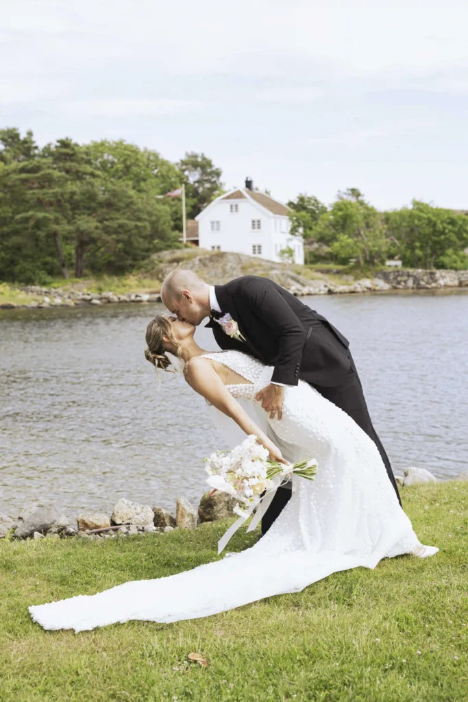 Brudgom dypper bruden i et romantisk kyss ved sjøen på Strand Hotel Fevik.