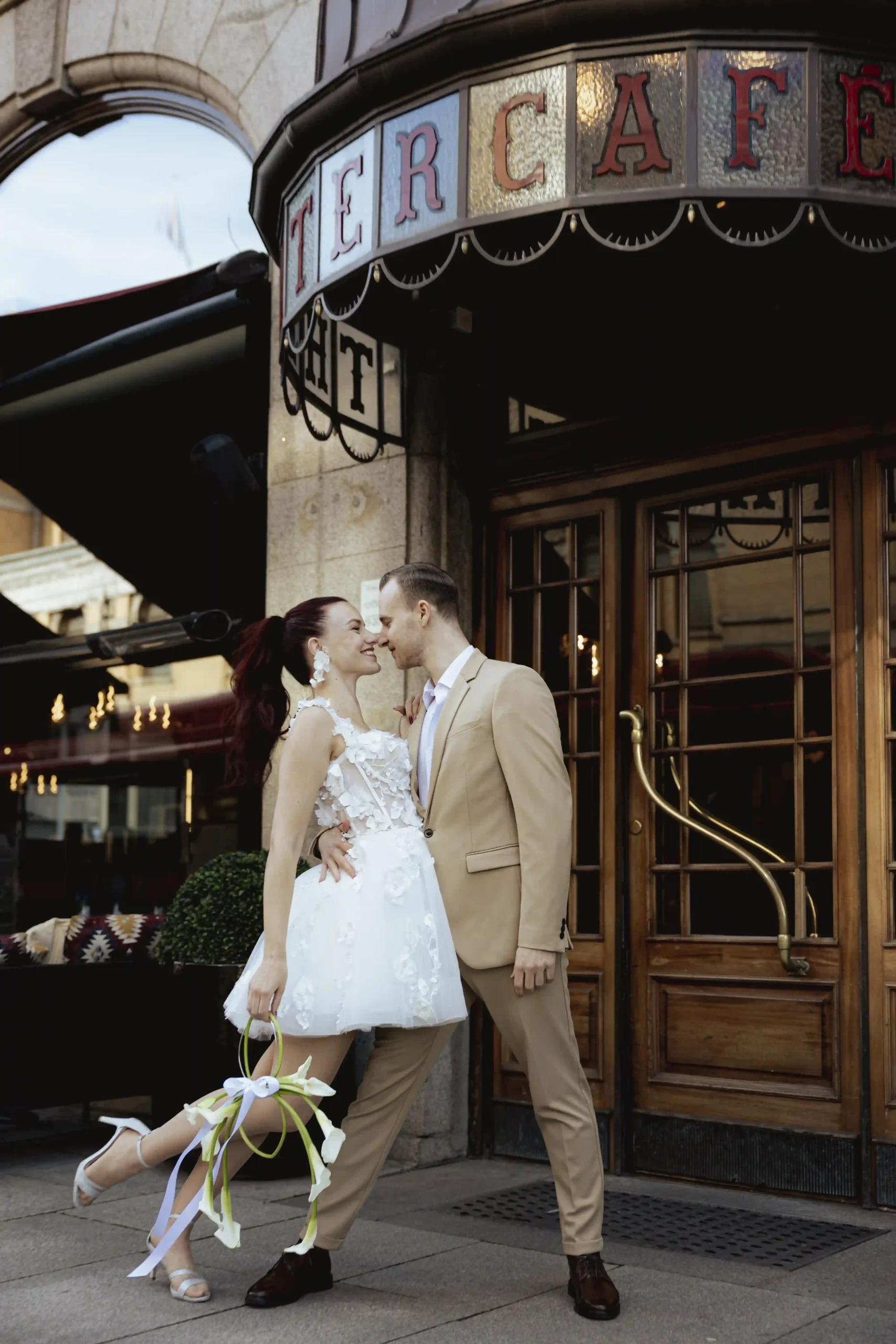 Elegant bride and groom sharing a kiss outside a historic café entrance during their intimate city elopement in Oslo — Anna O. Brambilla photography.” Elegant brudepar deler et kyss foran en historisk kaféinngang under sitt intime elopement i Oslo — fotografert av Anna O. Brambilla.