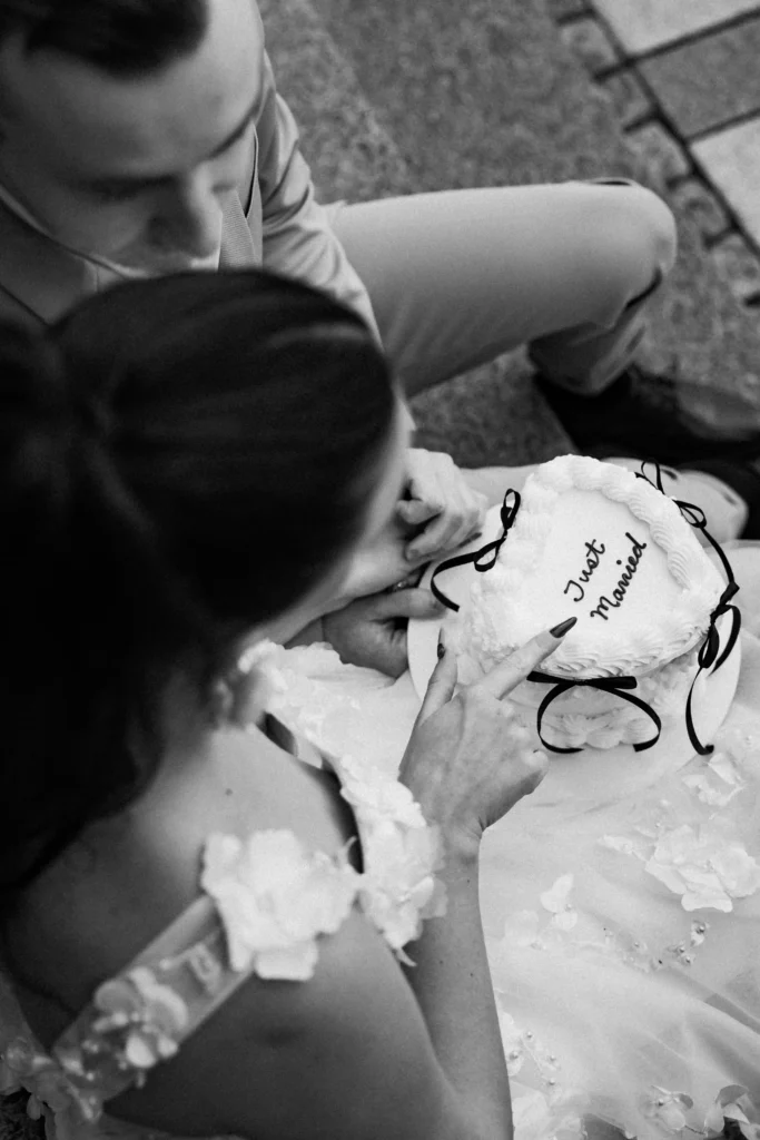 “Couple sitting close, holding a small ‘Just Married’ cake during their intimate city elopement in Oslo — Anna O. Brambilla wedding photographer.” “Brudepar som sitter tett sammen med en ‘Just Married’-kake under sitt intime elopement i Oslo — fotografert av Anna O. Brambilla.”