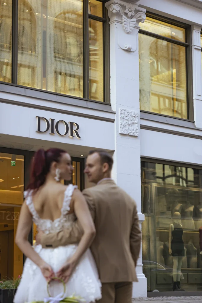 “Bride and groom outside Dior boutique during their stylish city elopement in Oslo — captured by Anna O. Brambilla.” “Brudepar utenfor Dior-butikken under sitt stilfulle elopement i Oslo — fotografert av Anna O. Brambilla.”