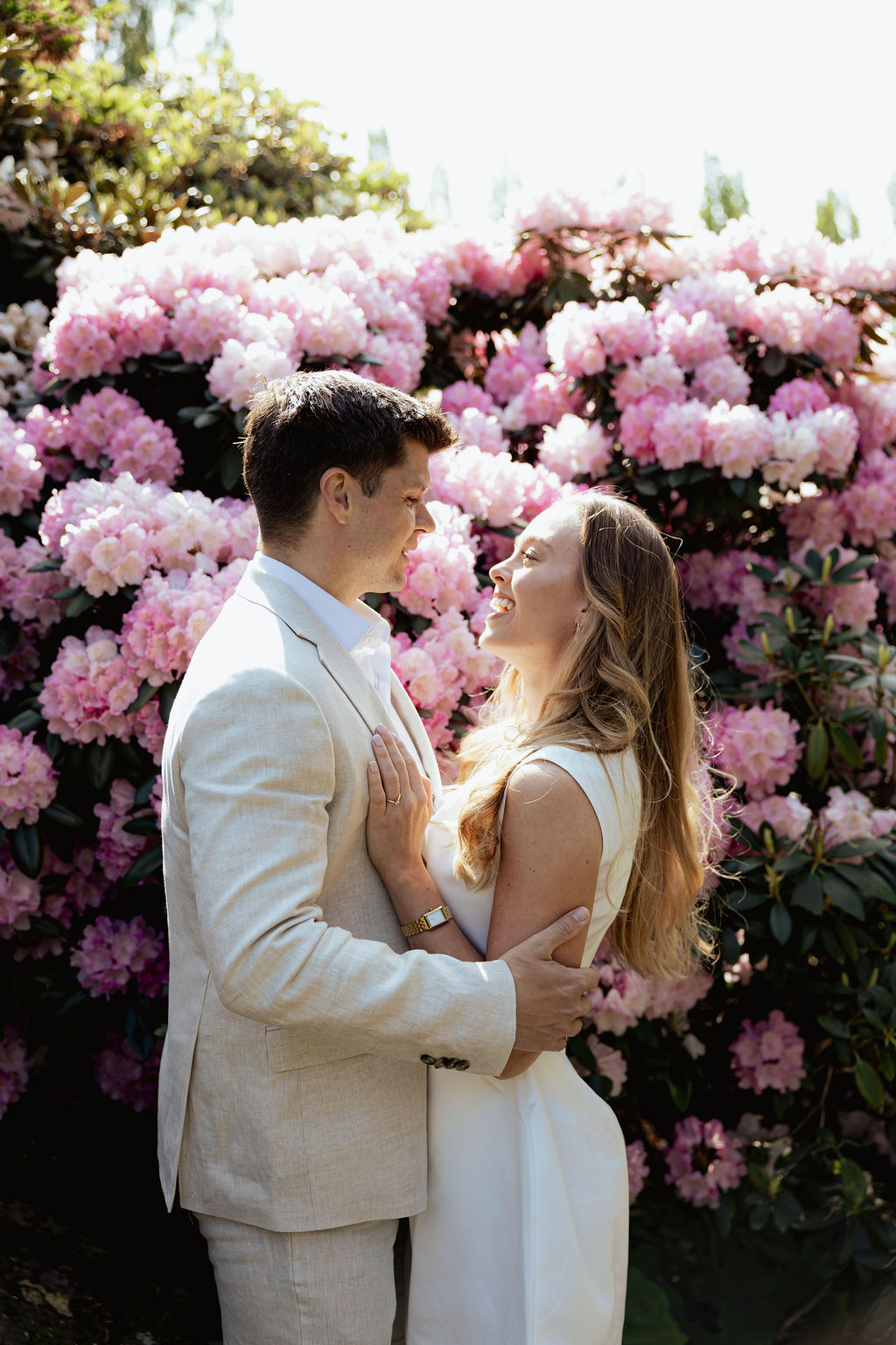 Forlovelsesfotografering i Botanisk Hage – par som ser på hverandre foran store rosa rhododendronbusker.