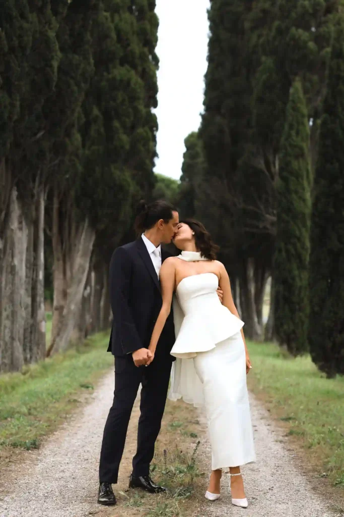 Brudepar som kysser på en allé med høye sypresser i Toscana