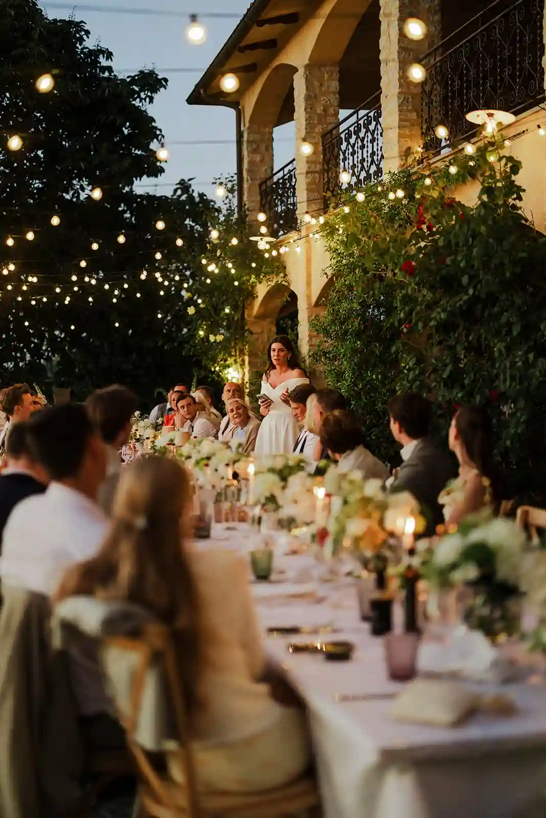 Gjester samlet rundt langbord under talene på bryllupsmiddagen i Toscana Guests gathered around the long table during speeches at the wedding dinner in Tuscany